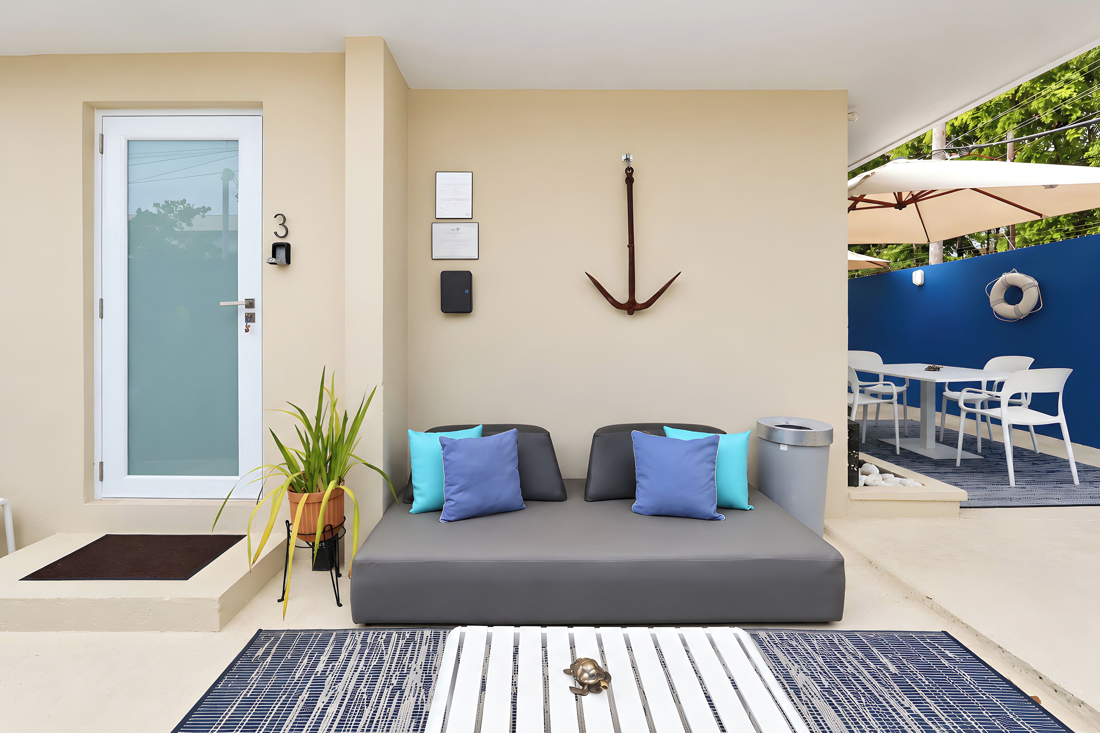 A modern living room with a sofa, cushions, a potted plant, a wall-mounted anchor decoration, and a door with a frosted glass panel.