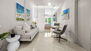 A modern living room with a sofa, a dining table, and a chair. There are paintings on the walls and a plant on the side table. - THE BUOY (San Juan)