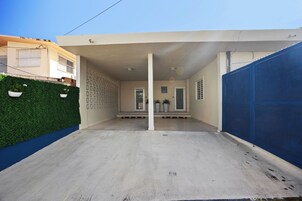 Una casa moderna con un porche cubierto, un seto verde y un portón azul.