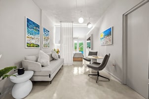 Una sala de estar moderna con un sofá, una mesa de comedor y una silla. Hay cuadros en las paredes y una planta sobre la mesita auxiliar.