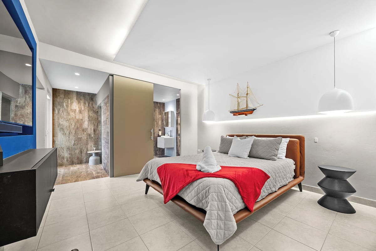 A modern bedroom with a bed, a red throw blanket, a ship decoration on the wall, and a unique black side table.