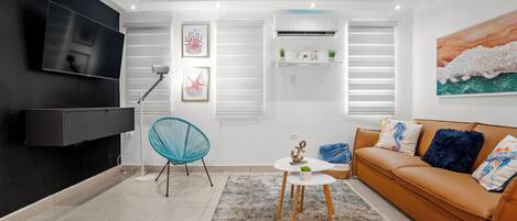 A modern living room with a flat-screen TV, a sofa, a coffee table, and a blue chair.