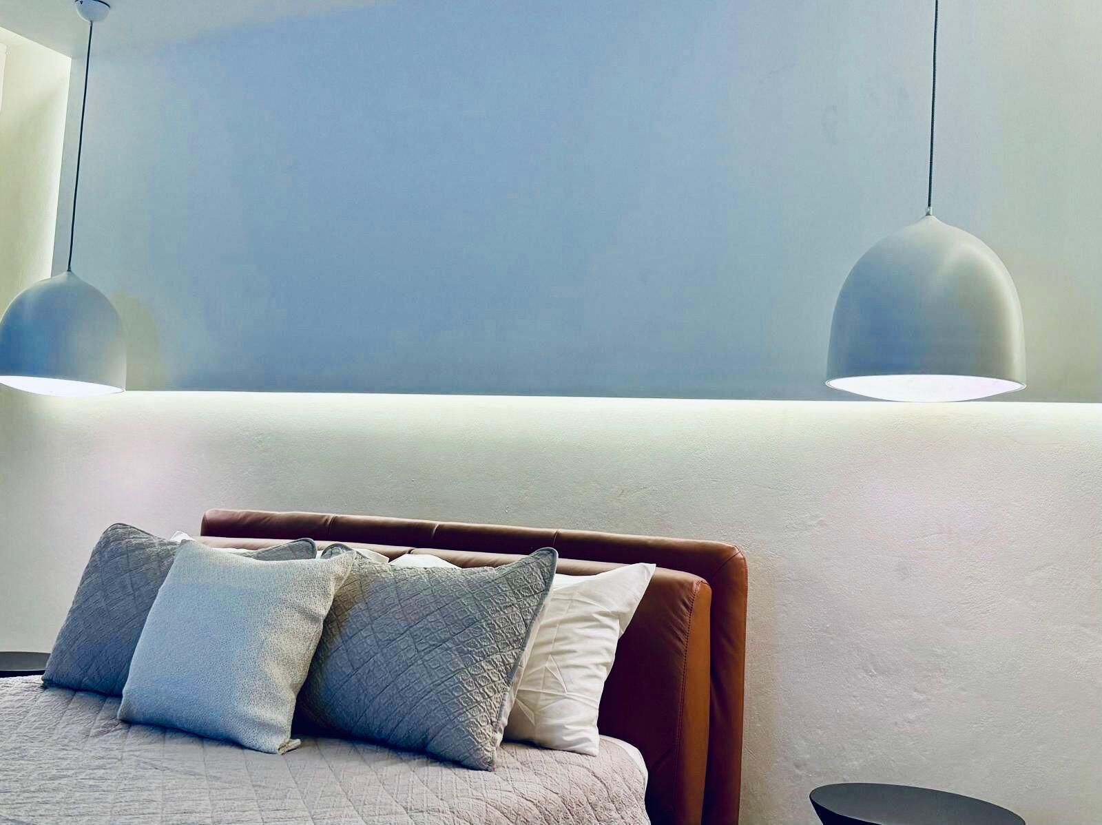 Een moderne slaapkamer met een bed, kussens en hanglampen.
