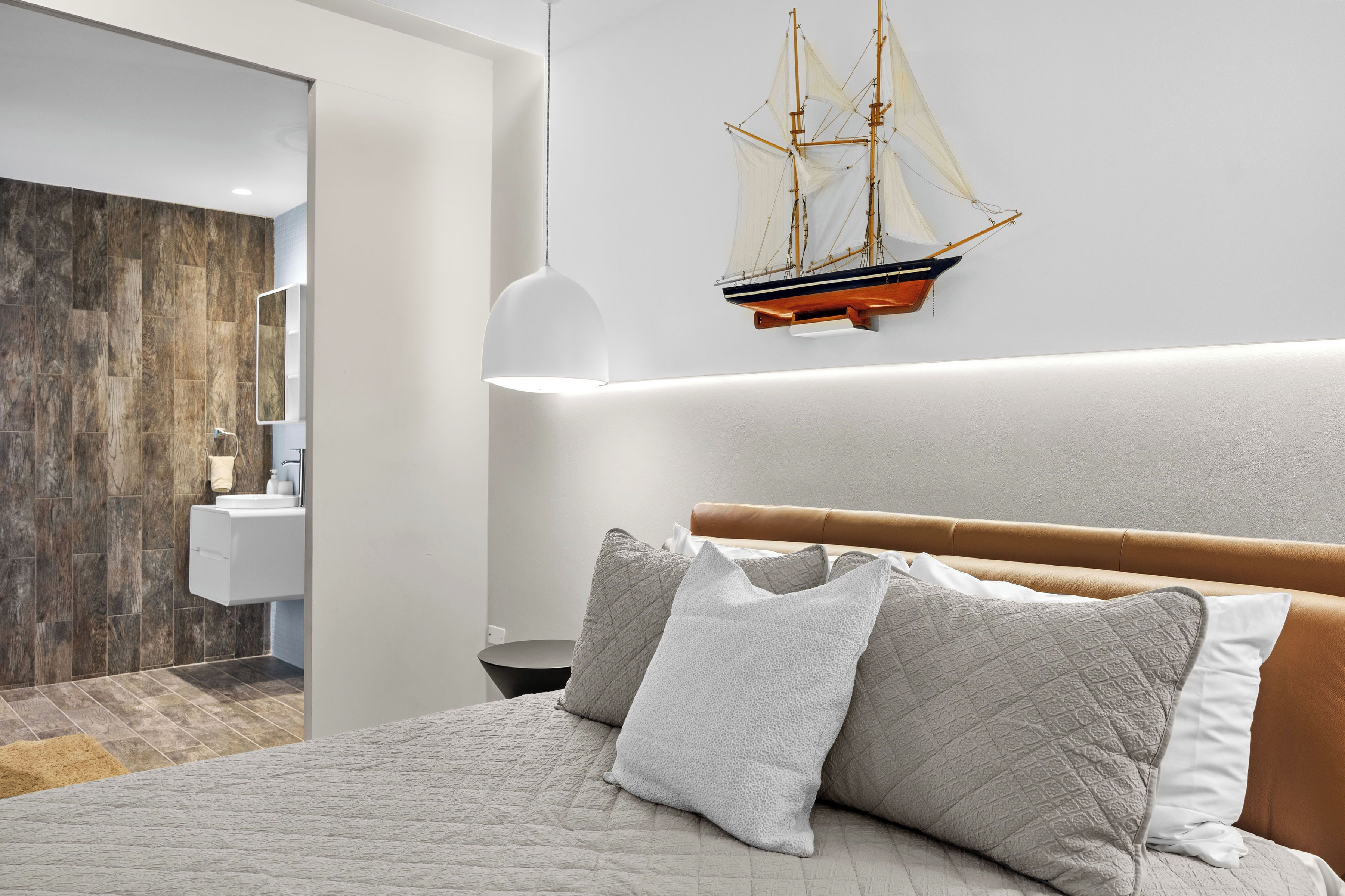 A modern bedroom with a large bed, a headboard, and a wall-mounted ship model.