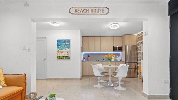 A modern kitchen with wooden cabinets, a stainless steel refrigerator, and a dining area with white chairs and a table. - THE BUOY (San Juan)
