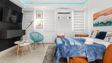 Ein modernes Schlafzimmer mit Bett, Fernseher, Sessel und Gemälde.
