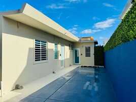 Un edificio moderno con techo plano, una pequeña entrada y una pared azul con seto verde.