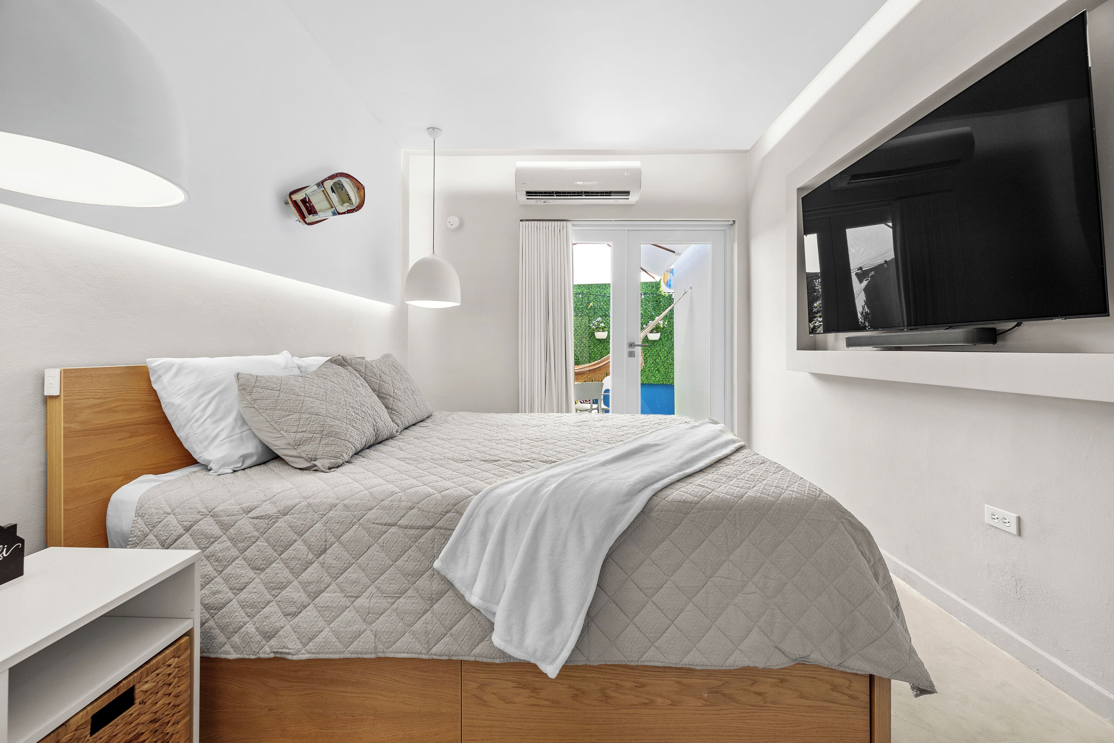 A modern bedroom with a bed, a TV, a ceiling light, and an air conditioning unit.