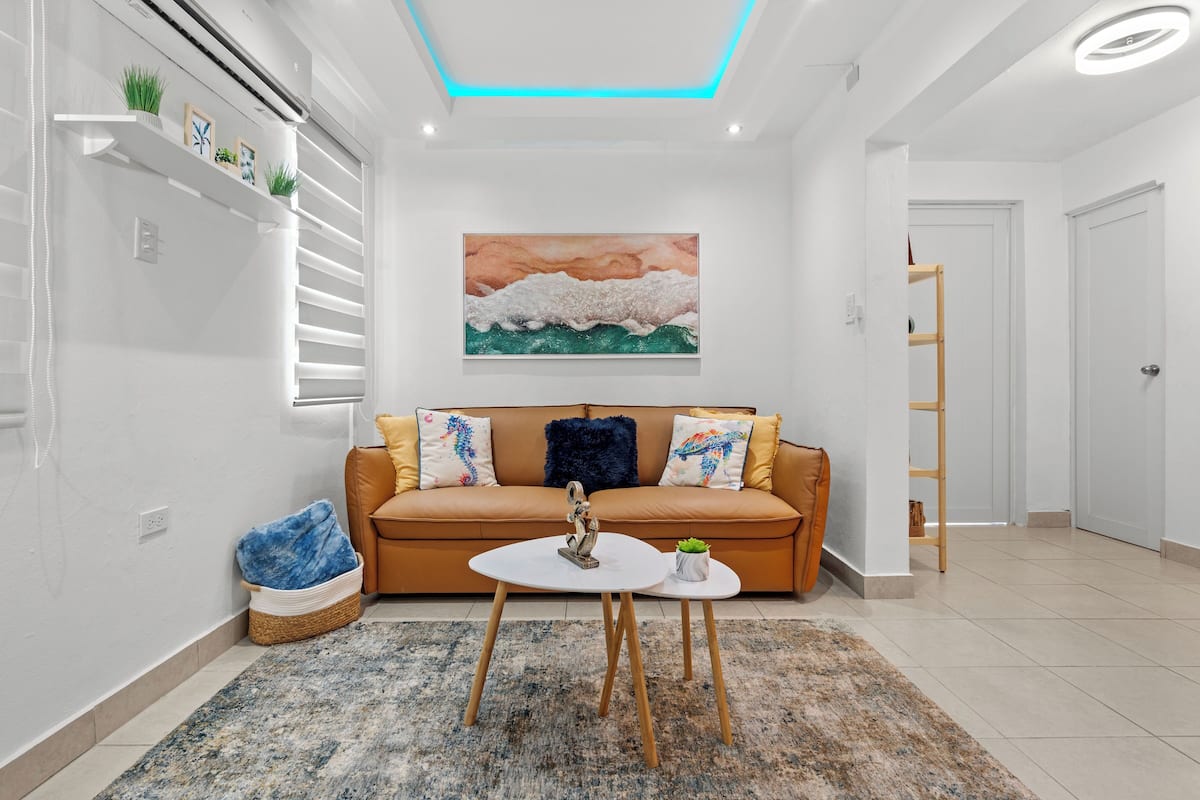 A modern living room with a sofa, a coffee table, a painting, and a ceiling light.
