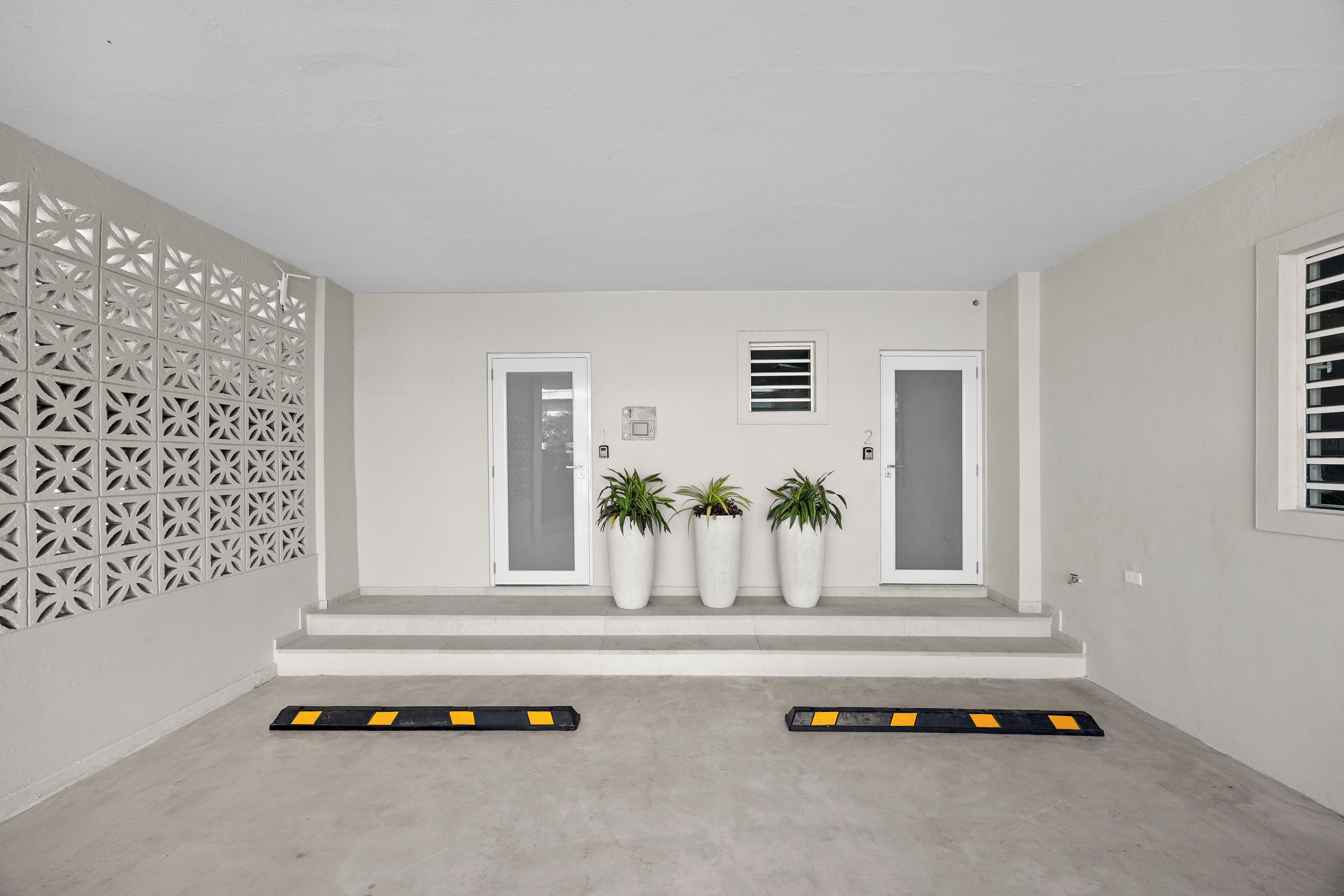 Una entrada limpia y moderna, con puerta blanca, plantas en macetas y un panel decorativo en la pared.