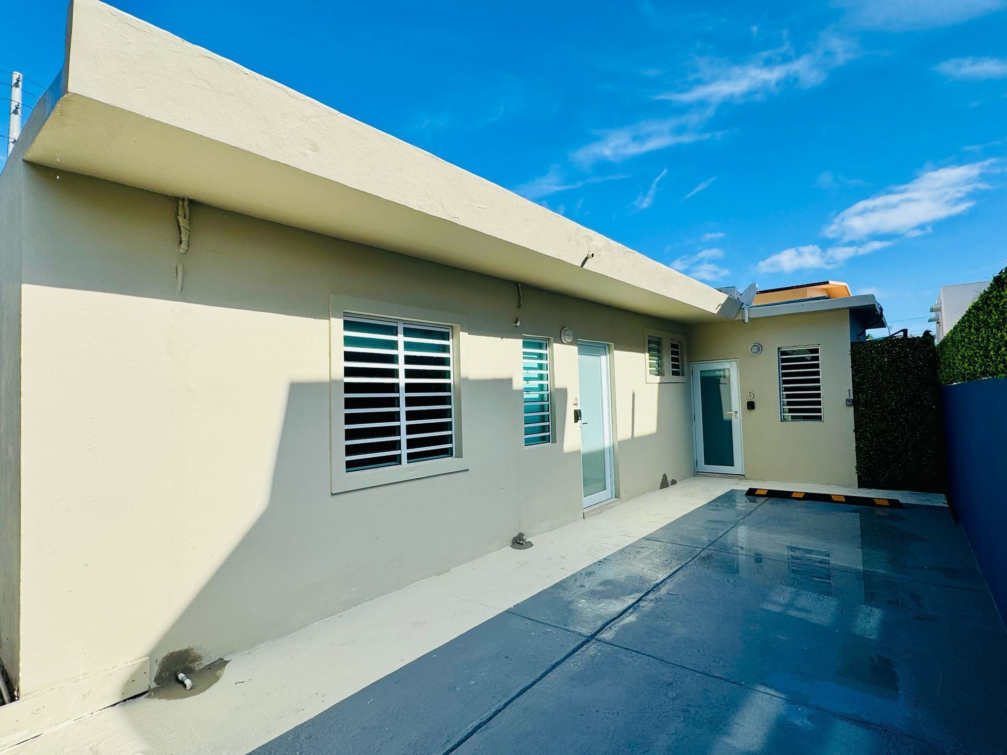 A building with a flat facade, multiple windows with blinds, and a paved entrance area.