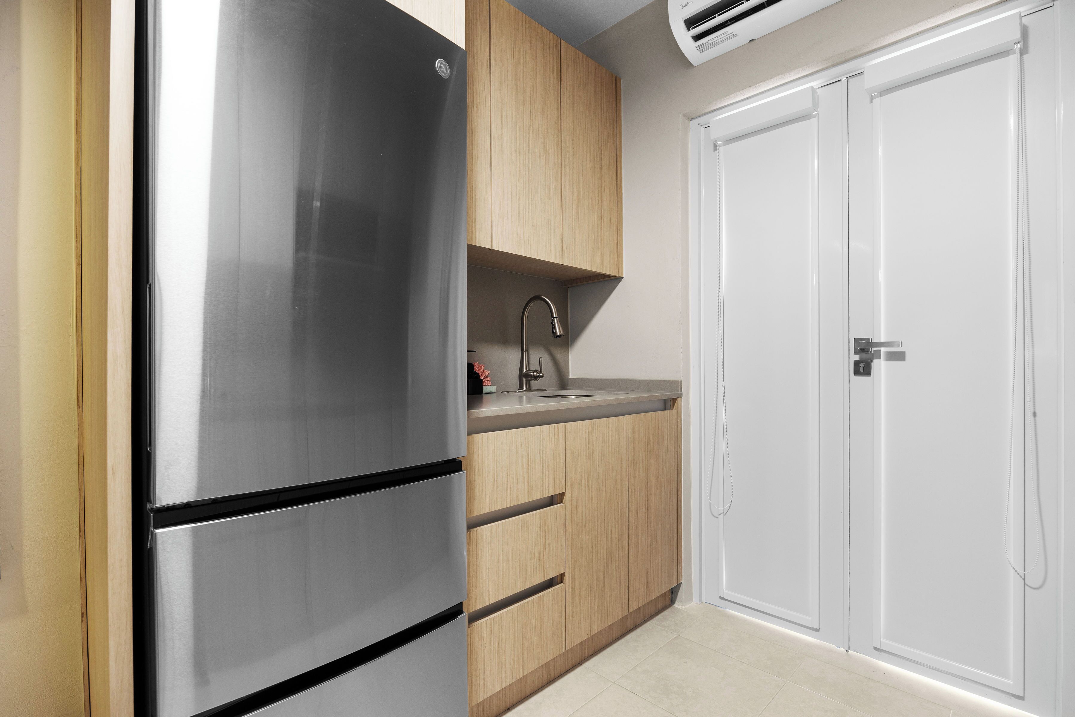 A kitchen with a stainless steel refrigerator, wooden cabinets, a sink, and a white door.