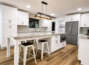 Una cocina moderna con armarios blancos, encimera de mármol y refrigerador de acero inoxidable.