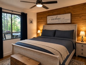 Une chambre à coucher avec un lit, des lampes de chevet, un ventilateur de plafond, une fenêtre avec des rideaux et un mur en bois.