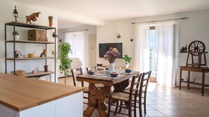 A spacious living area with a wooden dining table, chairs, a bookshelf, and a TV mounted on the wall.