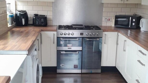 Cucina con pensili bianchi, cappa aspirante in acciaio inossidabile, forno doppio, microonde e lavatrice.