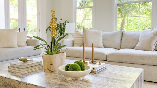 Una sala de estar moderna con una mesa de centro de mármol, un sofá y ventanas grandes con vistas a la vegetación.