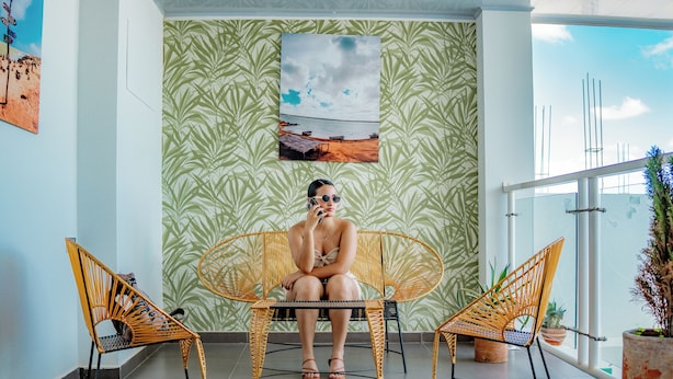 Ein Zimmer mit einem großen Fenster, einem Bild mit Strandmotiv und zwei Korbstühlen.
