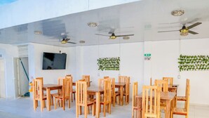 Ein geräumiger Essbereich mit Holztischen und -stühlen, Deckenventilatoren, einem Fernseher und grünen Wanddekorationen.