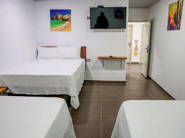 A hotel room with two beds, a television, a small table, and a door leading to another room. - El Cairo Hotel (Uribia)
