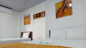 Ein Hotelzimmer mit einem großen Bett, zwei Einzelbetten, einem hölzernen Kopfteil, einer weißen Wand und einem Gemälde.