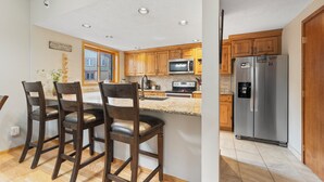 A modern kitchen with wooden cabinets, a stainless steel refrigerator, and a bar area with three stools. - Walk to town and slopes, family friendly 2-bedroom condo w/ WiFi in Breckenridge (Breckenridge)