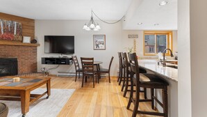 A modern living room with a fireplace, a flat-screen TV, and a dining area with wooden chairs and a table. - Walk to town and slopes, family friendly 2-bedroom condo w/ WiFi in Breckenridge (Breckenridge)