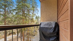 A balcony with a covered grill, a view of trees, and a wooden wall. - Walk to town and slopes, family friendly 2-bedroom condo w/ WiFi in Breckenridge (Breckenridge)