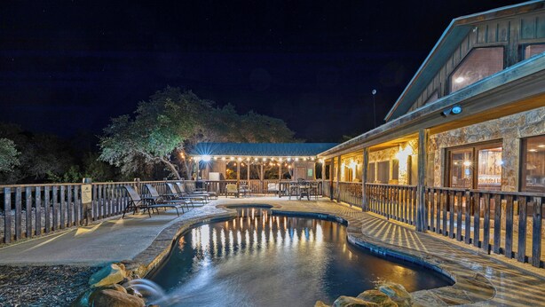 A nighttime view of a pool area with a wooden deck, lounge chairs, and a building with large windows. - La Mansion on The Frio - Pickleball Court, Pool (Concan)
