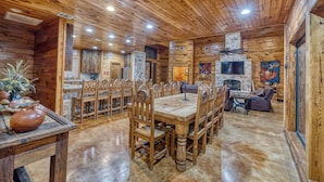 A wooden cabin interior with a dining area, stone fireplace, and a television. - La Mansion on The Frio - Pickleball Court, Pool (Concan)