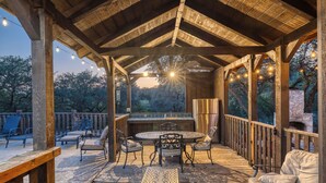 A covered outdoor patio with a wooden deck, a round table with chairs, and a seating area with a sofa. - La Mansion on The Frio - Pickleball Court, Pool (Concan)