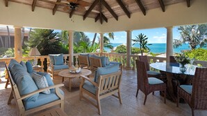 A covered outdoor seating area with wooden furniture and a view of the ocean. - Villa Caona, Quintessential Caribbean Oceanfront Home (Providenciales)