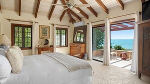 A bedroom with a large bed, wooden dresser, and a view of the ocean. - Villa Caona, Quintessential Caribbean Oceanfront Home (Providenciales)
