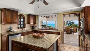 A kitchen with granite countertops, wooden cabinets, and a view of the ocean. - Villa Caona, Quintessential Caribbean Oceanfront Home (Providenciales)
