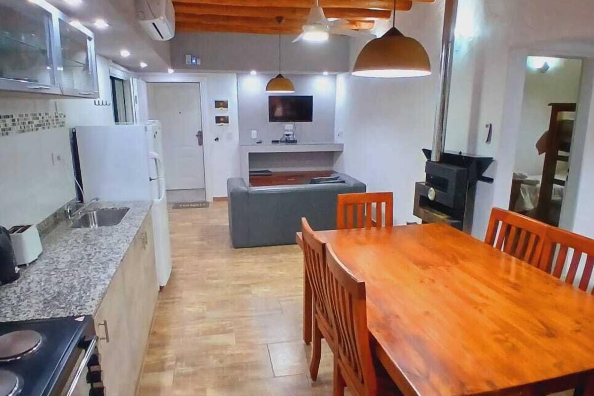 A compact kitchen with a stove, sink, and modern appliances. There is a dining area with a wooden table and chairs.
