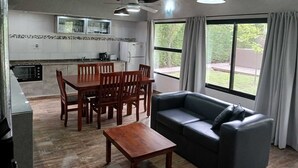 Ein kompakter Wohnbereich mit Essbereich, einer Couch, einer Küche mit Mikrowelle und einem großen Fenster mit Vorhängen.