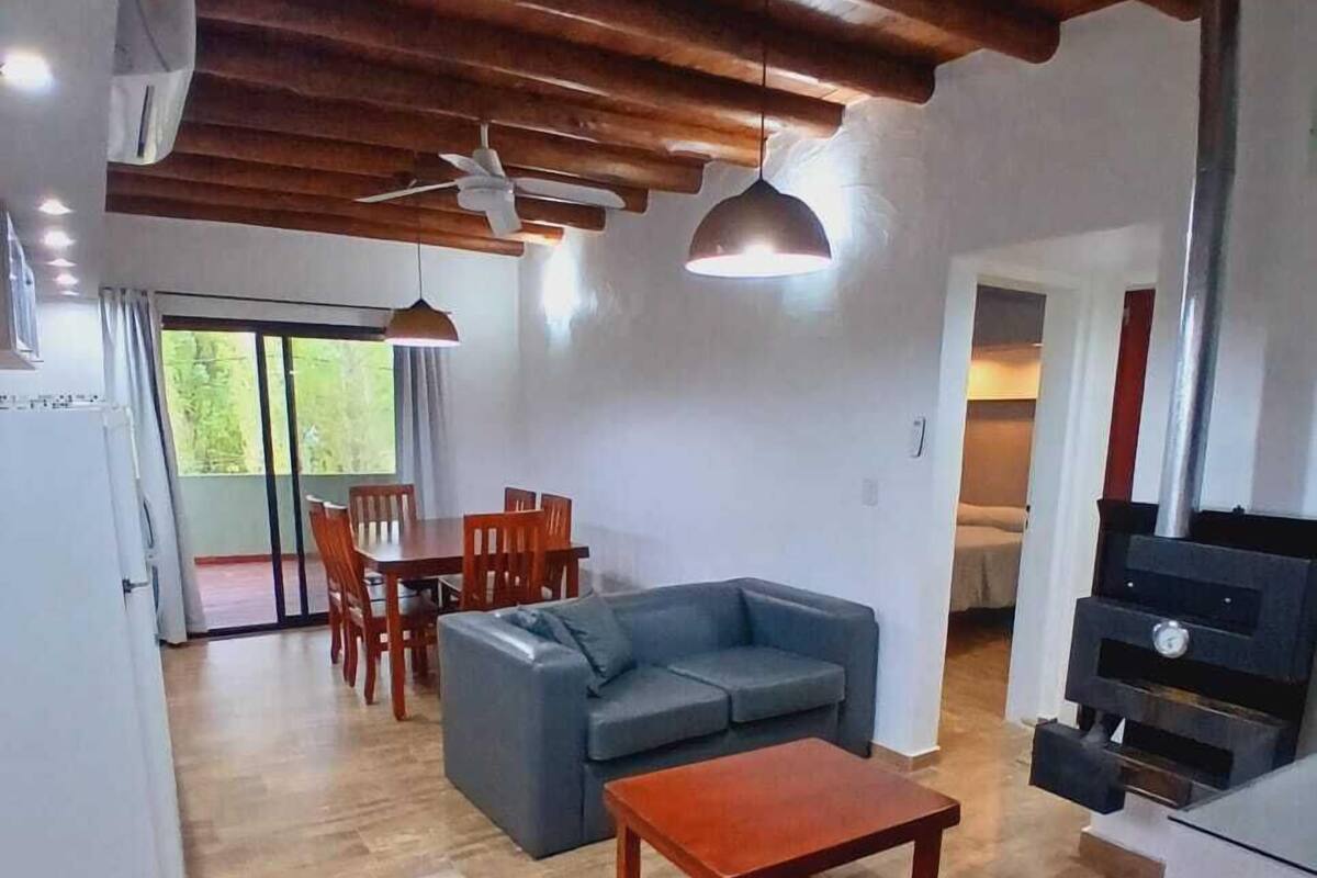 A spacious living area with a wooden ceiling, a gray sofa, a wooden coffee table, and a dining area with a table and chairs.