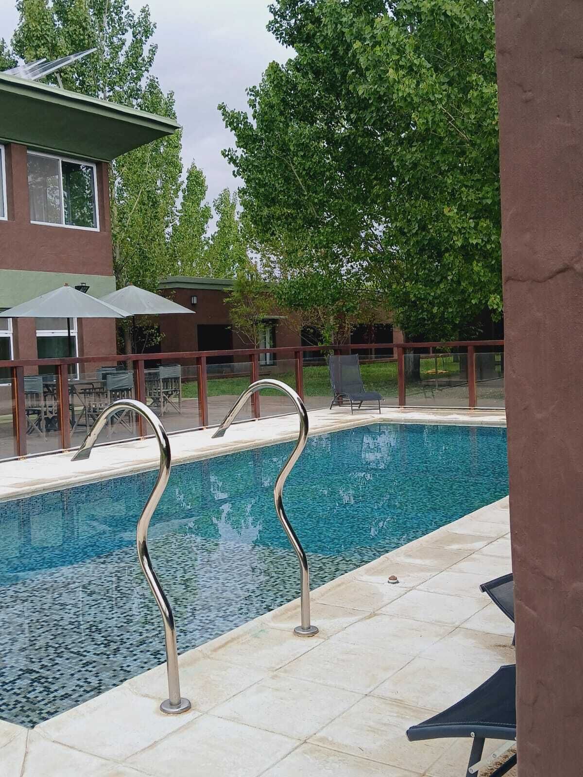 A swimming pool with a metal deck and lounge chairs, surrounded by a fence and trees.