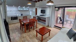 Ein geräumiger Wohnbereich mit einem Holzessttisch, einer Couch und einem Fernseher. Es gibt eine Küchenzeile mit einer Mikrowelle, einem Toaster und einem großen Fenster.