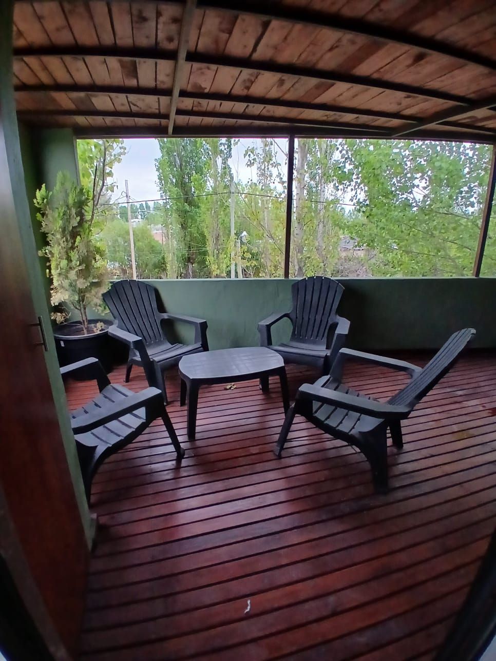 A covered outdoor seating area with a wooden deck, two lounge chairs, and a small table.