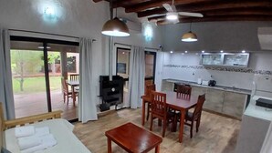 Ein gemütlicher Wohnbereich mit einer Couch, einem Holztisch und einem Esstisch mit Stühlen. Im Hintergrund ist eine Küche mit einem Fernseher und einem Grill zu sehen.