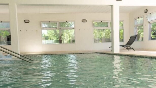 Ein Innenpool mit klarem Wasser, umgeben von weißen Wänden und Säulen, sowie ein einzelner Liegestuhl.