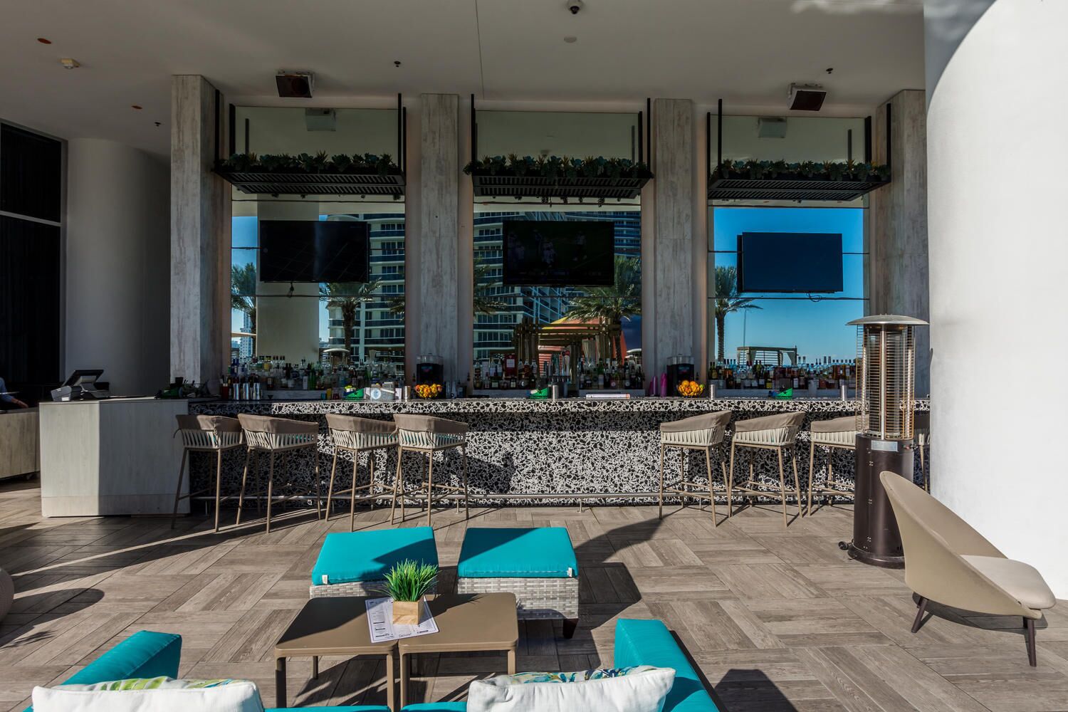 A modern outdoor bar area with a high ceiling, large windows, and a view of the cityscape.
