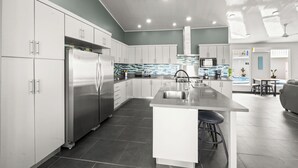Una cucina moderna con mobili bianchi, elettrodomestici in acciaio inossidabile e un'isola centrale con sgabelli.
