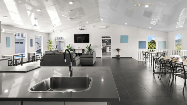 Una cucina moderna con isola centrale, un'area pranzo con tavolo e sedie rotonde, e un soggiorno con divano e televisore.