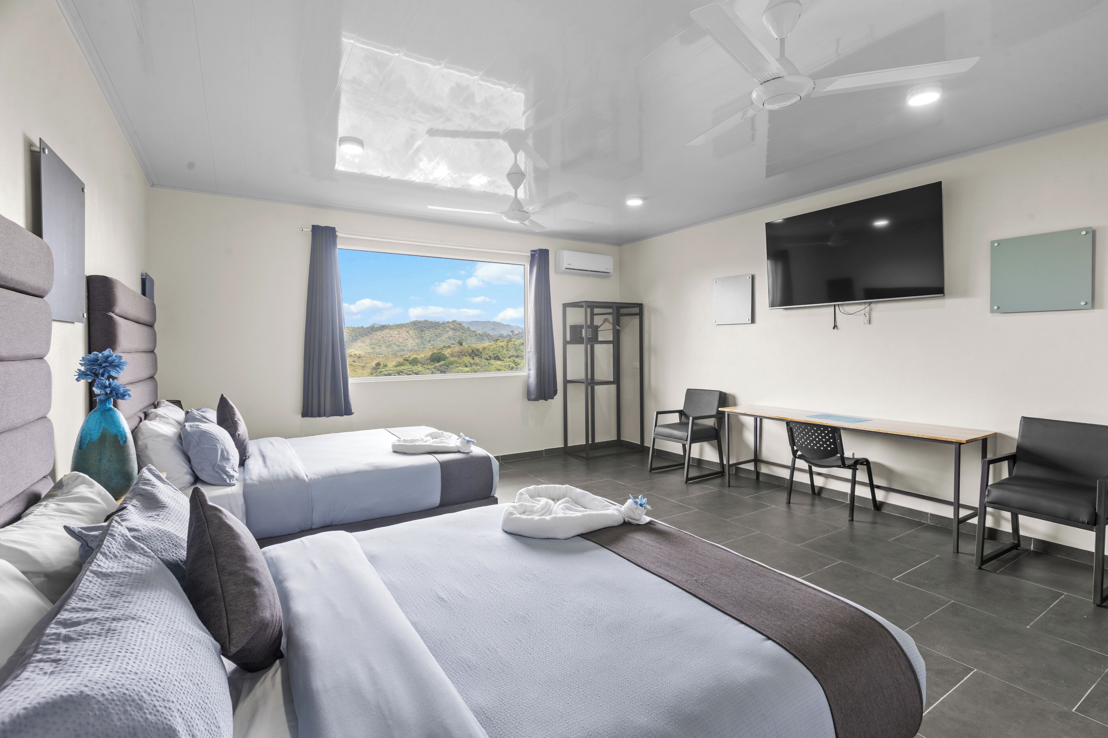 Una habitación de hotel moderna con dos camas, un escritorio, un televisor y vistas a las montañas.