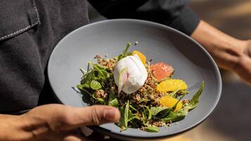 Una persona sosteniendo un plato con ensalada, que incluye hojas verdes, quinoa y un huevo escalfado.