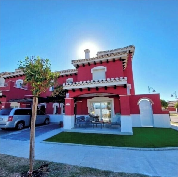 A red building with a tiled roof, a small patio with outdoor furniture, and a parked car in front. - Stunning 2 bed Villa With Private Salt Water Pool (Torre-Pacheco)