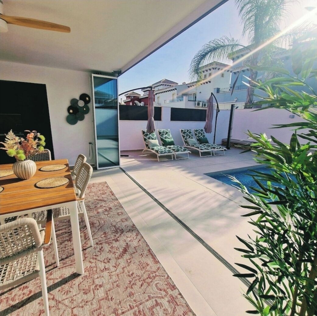 A modern outdoor patio with a dining area, lounge chairs, and a swimming pool.