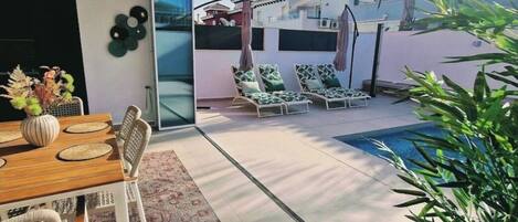 A modern outdoor patio with a dining area, lounge chairs, and a swimming pool.